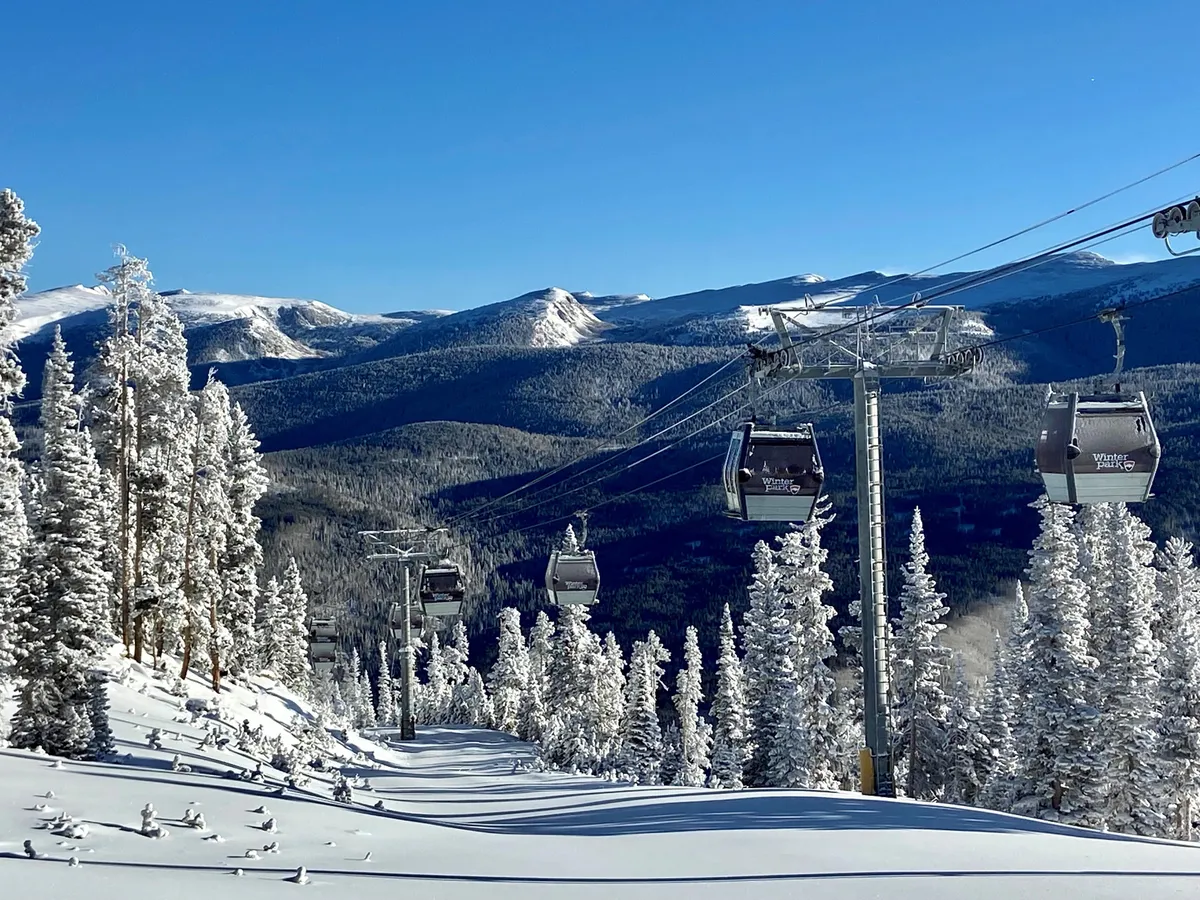 A stunning exterior view featuring a ski lift gliding above snow-covered trees, set against the backdrop of a majestic mountain landscape. The scene is alive with the excitement and tranquility of a high-altitude winter adventure.