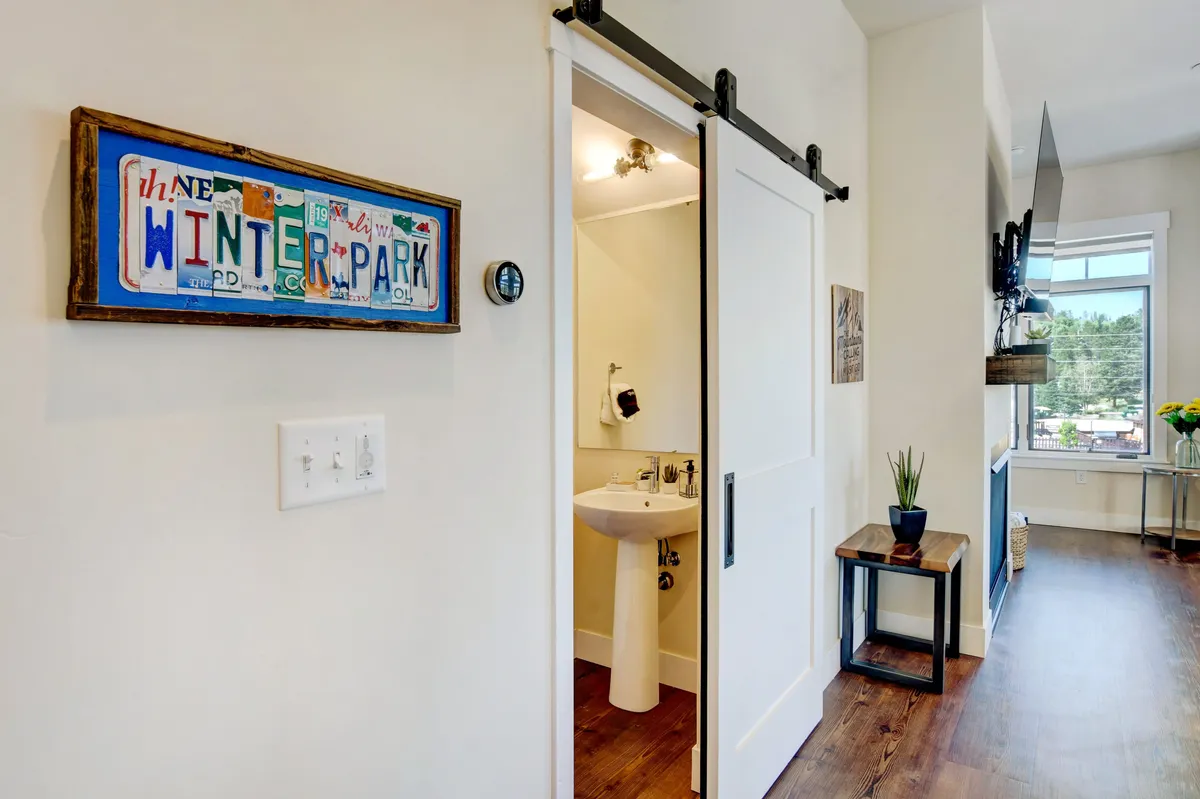 A welcoming interior entrance featuring a colorful sign, bathroom door, decorative plant, and a glimpse of the window. The layout subtly connects the indoors with the vibrant atmosphere outside, suggesting readiness for any adventure or season.