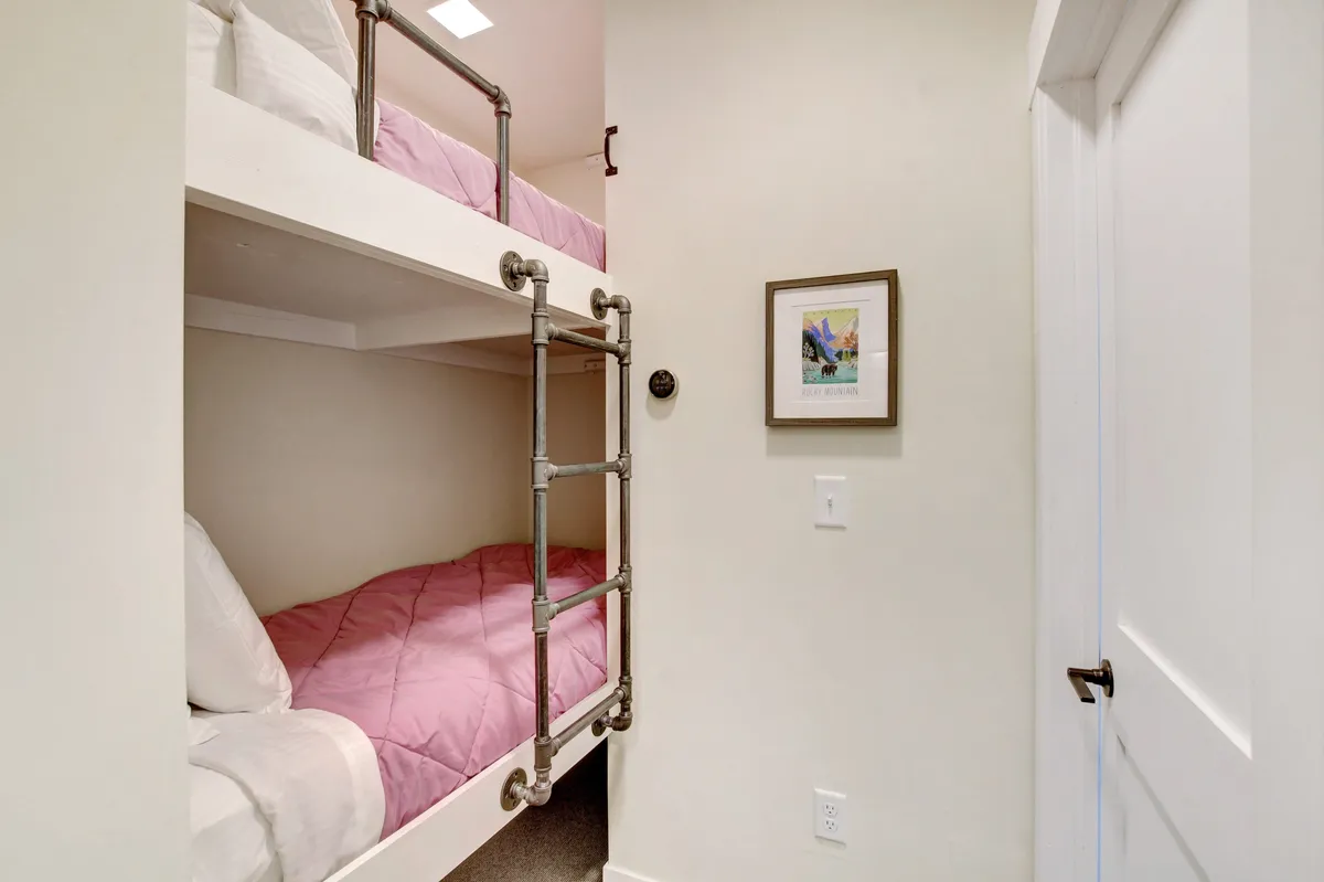 A playful and inviting bunk room featuring two bunk beds with ladders, framed artwork, and a comfortable setting for children or extra guests. The space feels intimate and ideal for family stays.