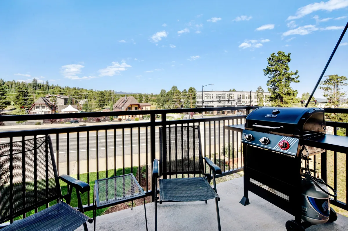 An exterior shot from the balcony, featuring comfortable chairs and a gas grill positioned to enjoy panoramic views of the mountain landscape. The scene is set for al fresco dining, morning coffee, or relaxing after a day of adventure, perfectly capturing the outdoor living experience.