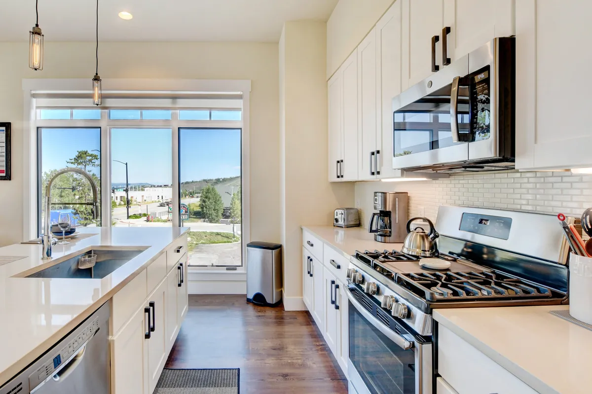 A bright, open-plan living and kitchen area featuring a large window that frames expansive mountain views. The modern kitchen includes stainless steel appliances and an island with a built-in sink, ideal for gathering and entertaining. Comfortable seating and a welcoming atmosphere make the space perfect for socializing.