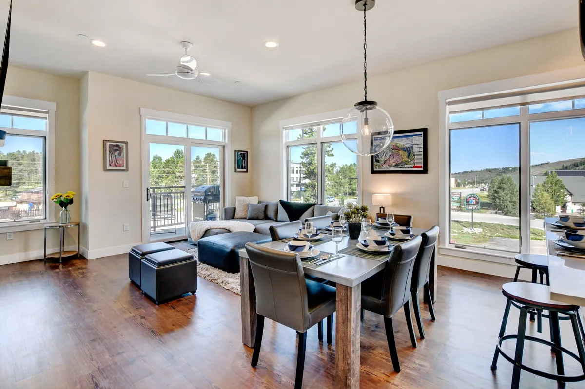 A light-filled living and dining area with a comfortable sectional sofa, a dining table set for a meal, and large windows that offer scenic mountain views. The space feels welcoming and ready for gatherings, no matter the season.
