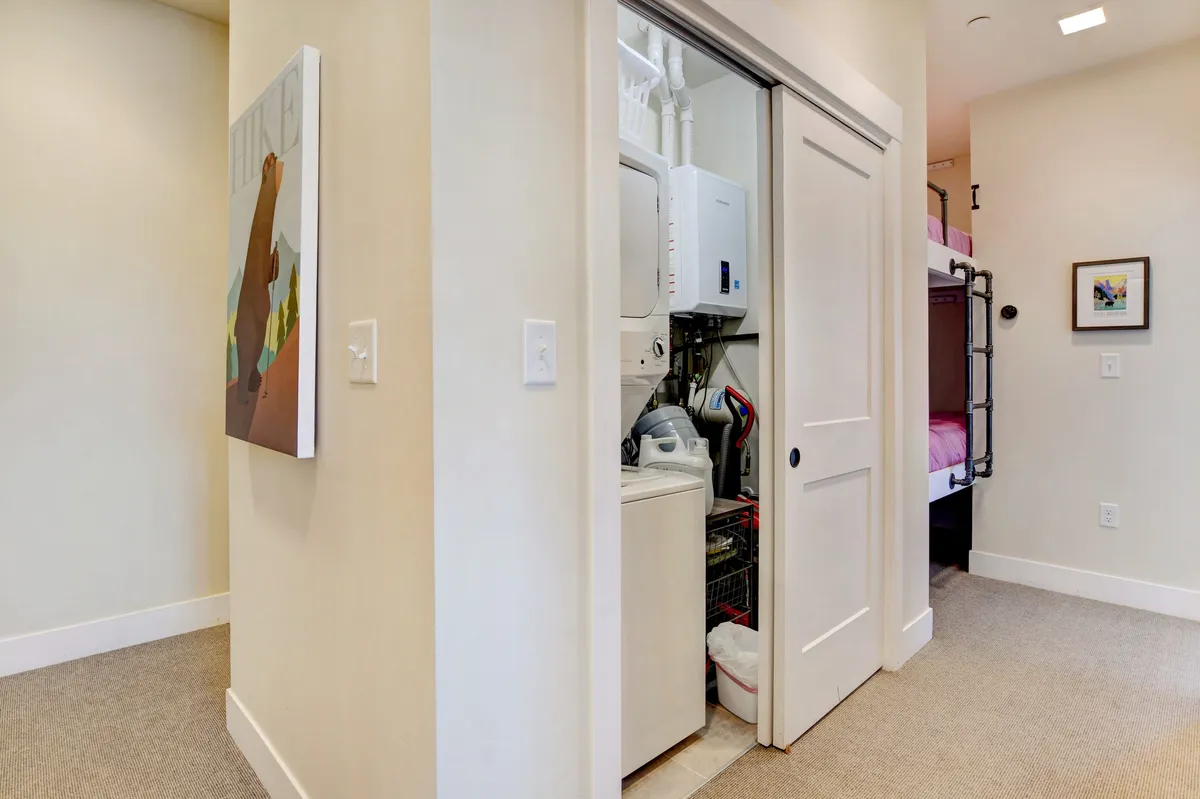 A cozy interior nook featuring modern laundry appliances neatly tucked beside bunk beds, with cheerful wall art adding a welcoming feel. The space is bright, practical, and designed to make chores comfortable and convenient.