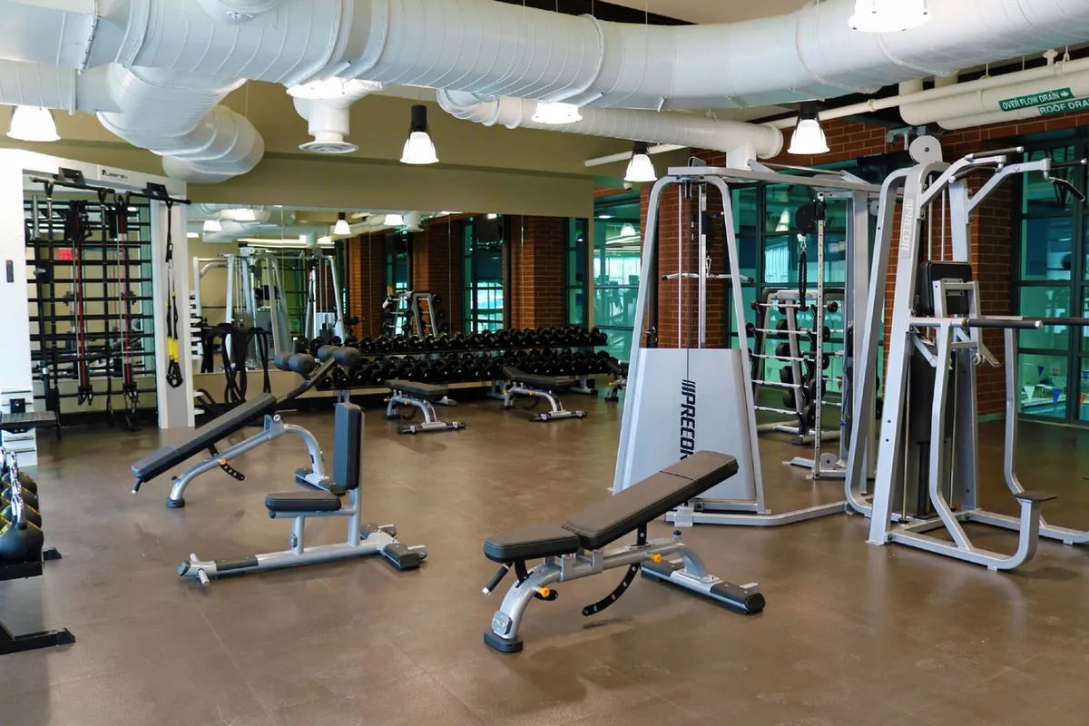 A modern, well-equipped fitness center with weight benches, dumbbell racks, exercise machines, and mirrored walls designed to support active lifestyles and post-adventure recovery.