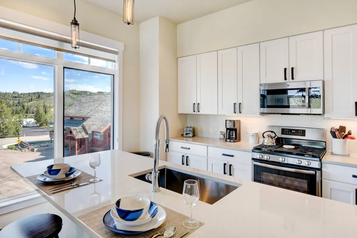 A welcoming chef's kitchen featuring a central island, modern stainless steel appliances, and large windows letting in natural light. The setting exudes warmth and is clearly designed for both cooking and socializing, with ample countertop space and a view perfect for starting the day.