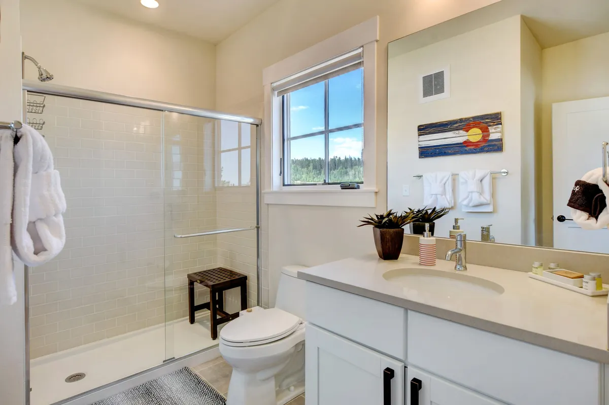 A calming bathroom filled with natural light, featuring a glass shower, modern vanity with sink, decorative wall art, and a window with a scenic view. The vibe is fresh, tranquil, and spa-like.